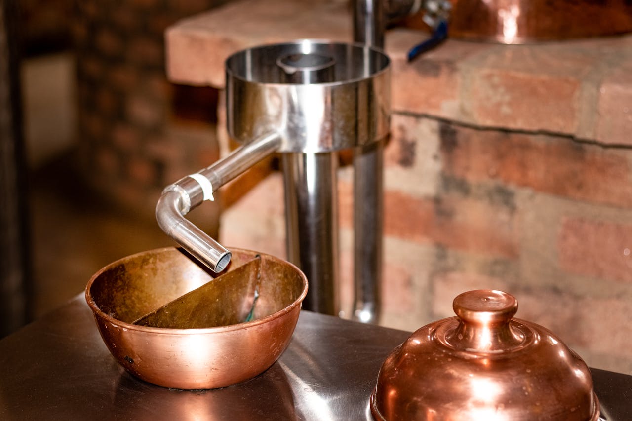 Close-up of copper distillation apparatus against a rustic brick background, indoors.