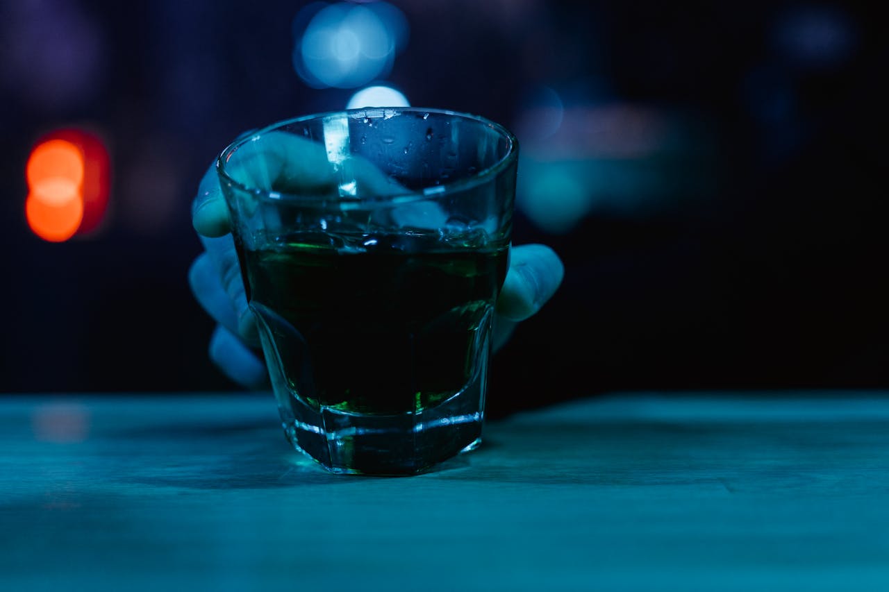 A close-up shot of a hand holding a glass with a drink in a dimly lit bar setting.