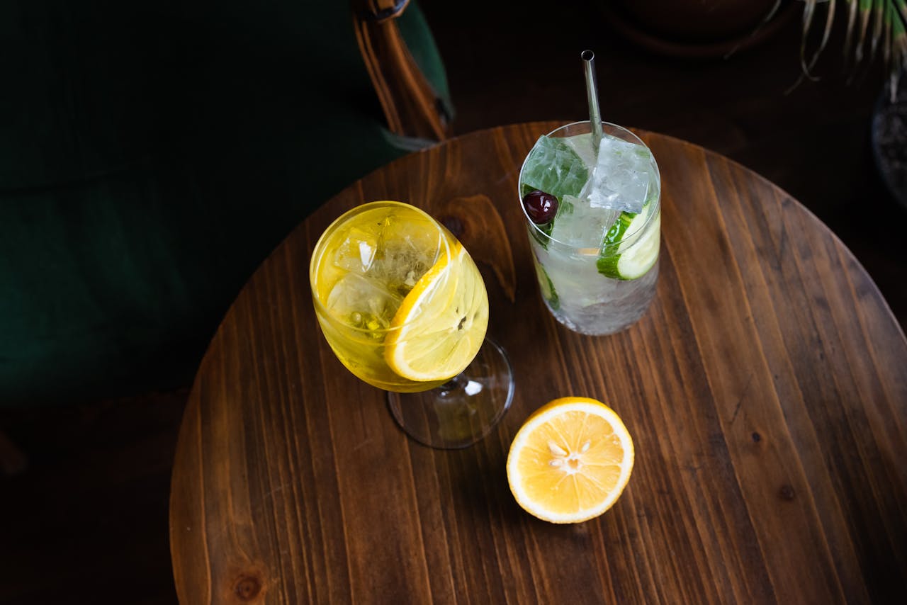 Overhead view of cocktails with lemon and cucumber garnishes on a wooden table.
